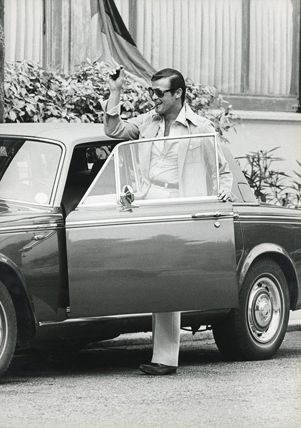 Tirage argentique en noir et blanc. Tout le glamour de James Bond dans cette image de format 21 x 29,7 cm représentant Roger Moore sortant de sa voiture.